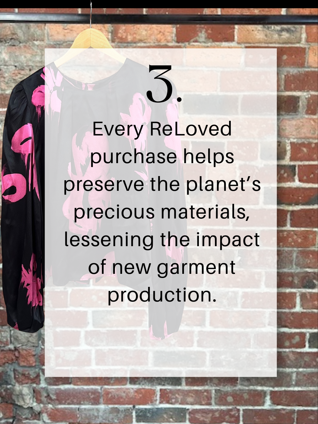 A pink and black floral blouse hanging on a wooden hanger